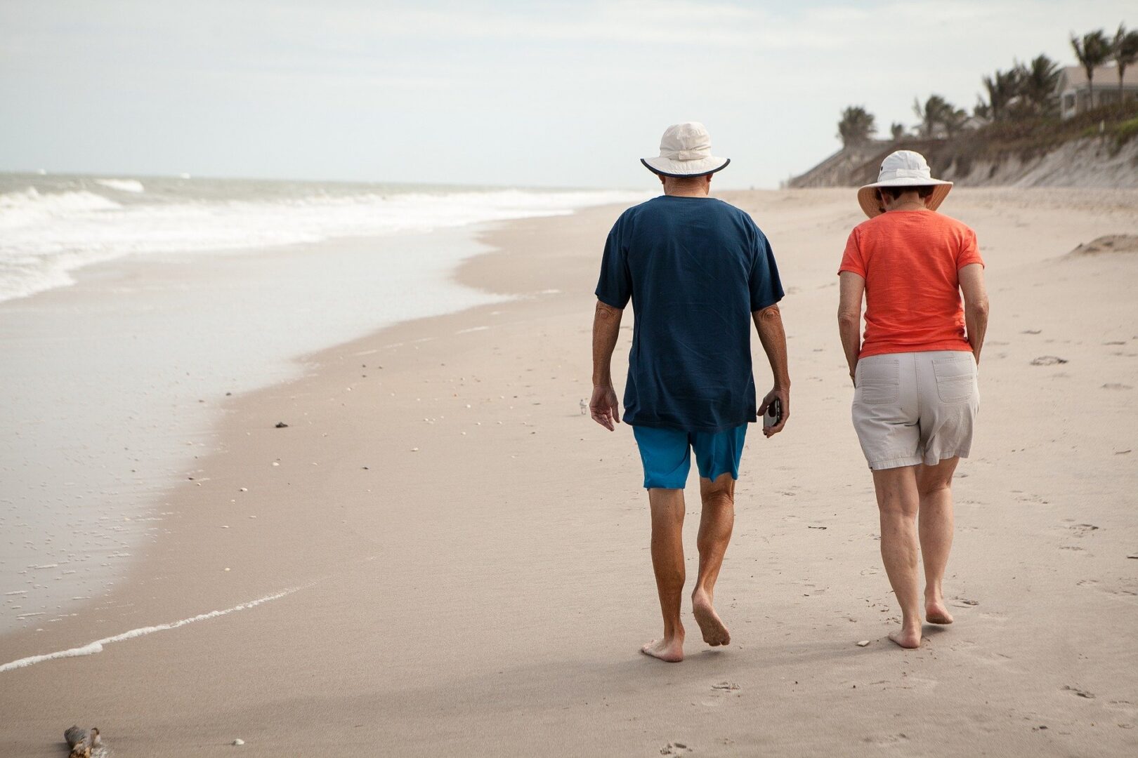 Elderly couple walking on a sandy beach.