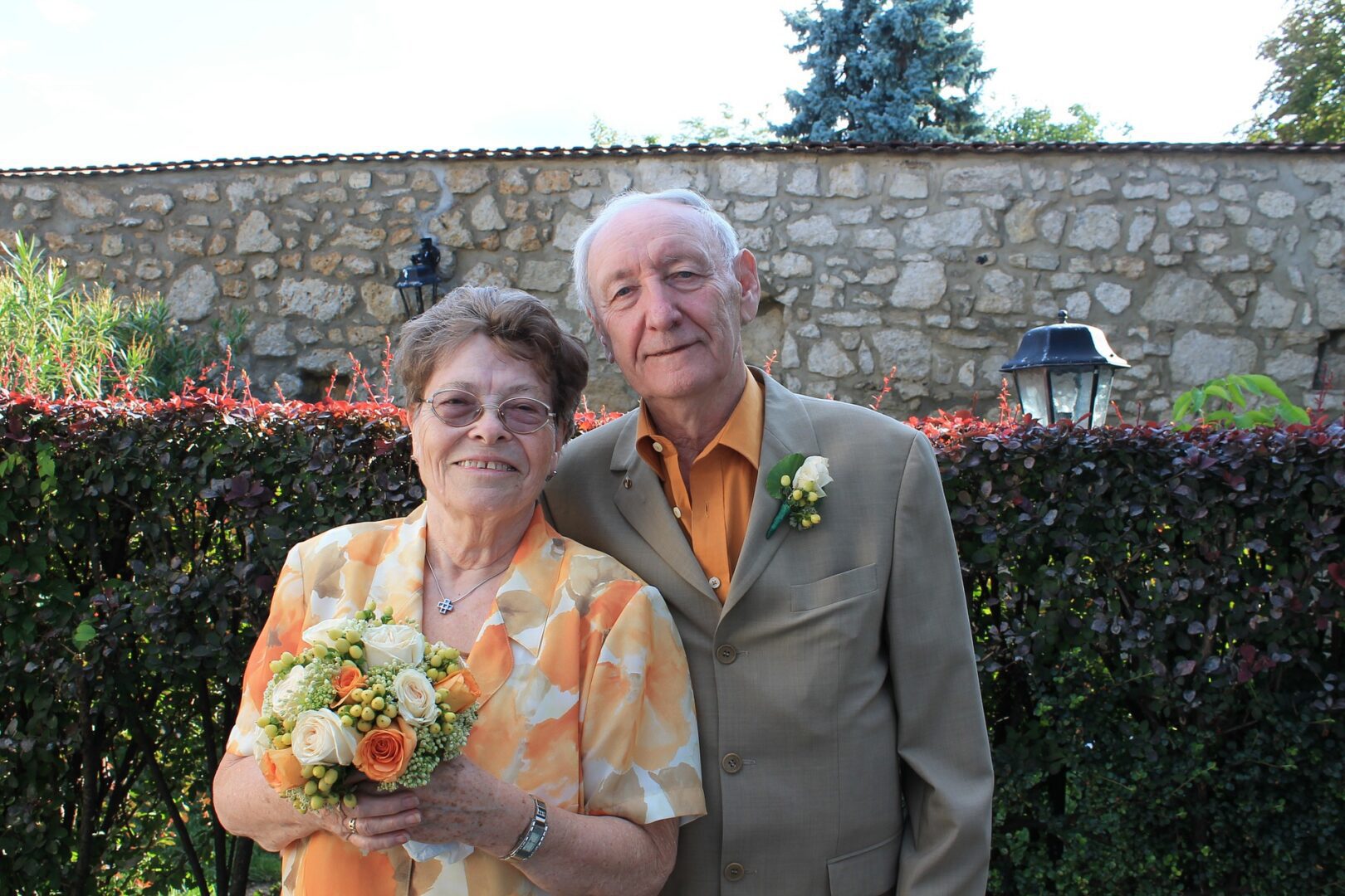 Elderly couple smiling with bouquet outdoors.