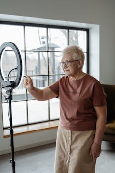 Elderly woman interacts with ring light, embracing modern technology indoors.