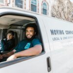 Two movers smiling from their moving company van parked on a sunny day.