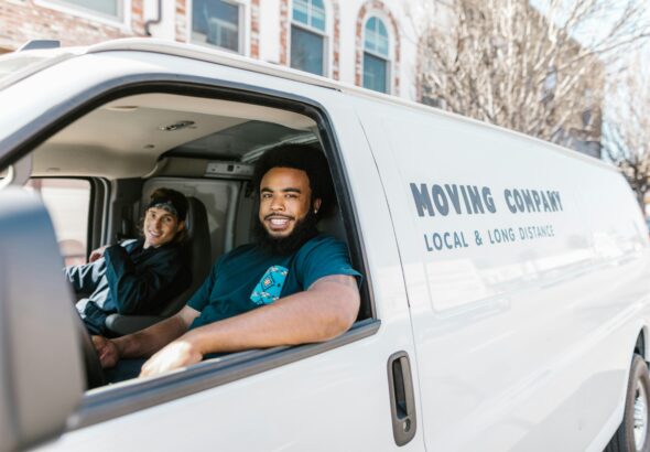 Two movers smiling from their moving company van parked on a sunny day.