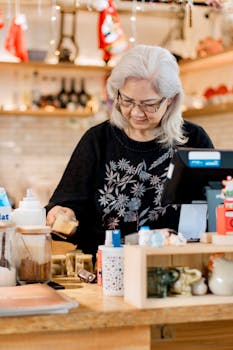 Elderly woman preparing drinks in a cozy coffee shop setting with warm ambiance.
