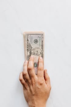 Top view of crop faceless person investing pile of American dollar banknotes on white table