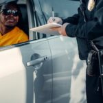 A police officer writes a ticket for a driver in a car during a roadside stop.