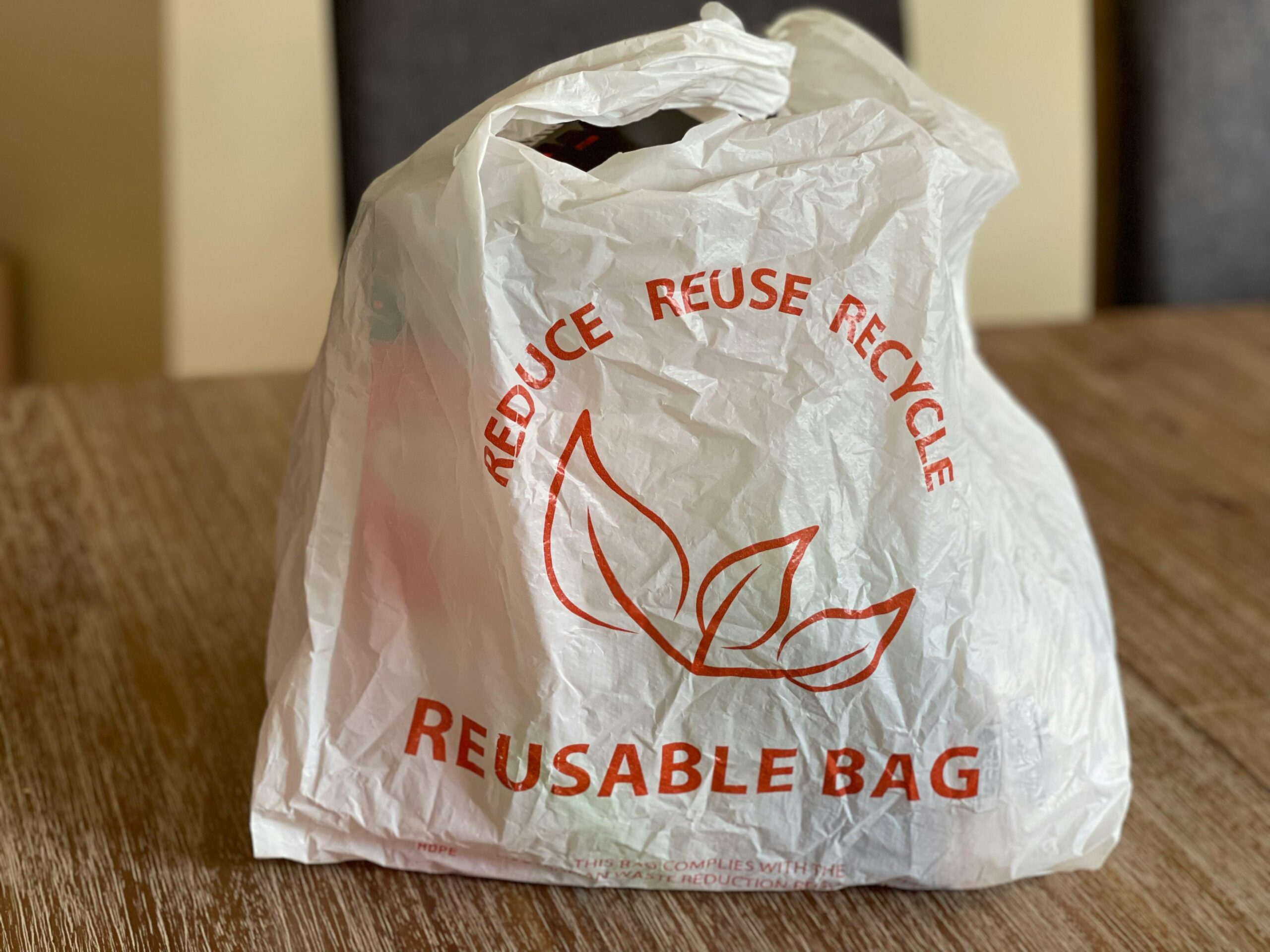 Reusable bag promoting reduce, reuse, recycle on a wooden table indoors.