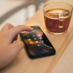 Close-up of hand unlocking a smartphone next to a cup of tea on a wooden table, emphasizing technology and security.